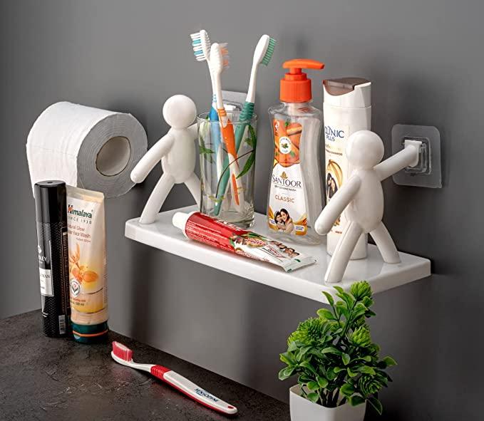 A bathroom shelf with dental hygiene products is featured in the image. Toothbrushes, toothpaste tubes, and other items are arranged on the light-colored wooden shelf mounted against a white-tiled wall. The toothbrushes come in different colors and bristle types, while the toothpaste tubes are of various brands and sizes. Some containers holding dental floss and other items are also visible. The image promotes dental hygiene in a well-organized bathroom setting.